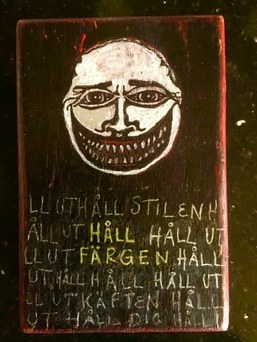 Mörkt konstverk med ett tecknat ansikte och handskriven text