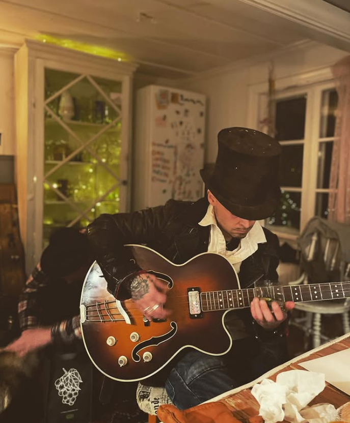 Dan Viktor spelar gitarr inomhus, i svart hatt och varm kvällsbelysning